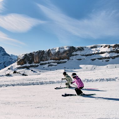 Two children skiing on a snowy slope in front of a mountain landscape in Kleinwalsertal, under a blue sky with clouds. | © Kleinwalsertal Tourismus eGen • Photographer: Oliver Farys