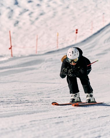 A child skiing on a slope, wearing a helmet and ski goggles, in a snowy winter landscape. | © Kleinwalsertal Tourismus eGen • Photographer: Oliver Farys
