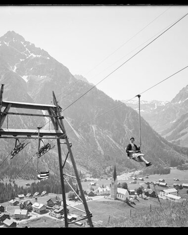 Historic photo of a ski lift in a valley, with mountains in the background and small buildings in the foreground. | © Kleinwalsertal Tourismus eGen • Karl Max Kessler Archiv