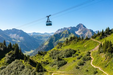 Bergbahn fährt über grüne Hänge und Berge im Kleinwalsertal, mit einem klaren blauen Himmel im Hintergrund. | © Oberstdorf · Kleinwalsertal Bergbahnen