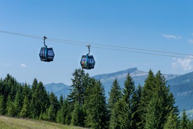 Zwei Kabinen einer Seilbahn hängen über einer grünen Baumlandschaft, mit Bergen im Hintergrund, bei Sonnenwetter. | © Oberstdorf · Kleinwalsertal Bergbahnen