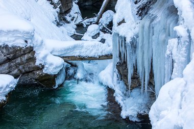 Stream in Breitachklamm during winter, surrounded by frozen water and snow, with ice-covered rocks and icicles. | © Kleinwalsertal Tourismus eGen • Breitachklamm • Photographer: Frank Drechsel