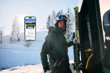 A skier with a helmet and skis stands next to a vehicle in a snowy winter landscape, with trees and mountains in the background. | © Kleinwalsertal Tourismus eGen