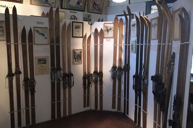 Ski museum display with antique skis mounted on a white partition wall at Walserhaus. | © Kleinwalsertal Tourismus eGen