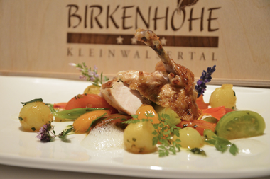 Gedeckter Teller mit gewürztem Fleisch, Gemüse und Saft, mit Kräutern und Lavendelblüten als Dekoration. | © Kleinwalsertal Tourismus eGen • Birkenhöhe