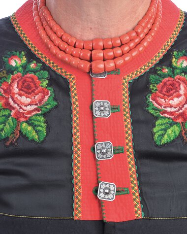 Nahaufnahme einer traditionellen Tracht, sichtbarer Rücken, mit roten und schwarzen Elementen, Stickereien und Knöpfen, inklusive roter Halskette. | © Kleinwalsertal Tourismus eGen • Fotograf: Christoffer Leitner