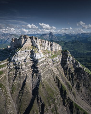 Mountain landscape with steep cliffs and green slopes under a cloudy sky. | © Kleinwalsertal Tourismus eGen • Photographer: Robert Niederwolfsgruber