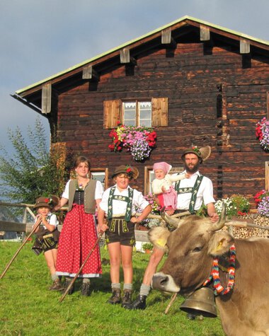 Familie in Trachten vor einer Holzalm mit Kühen und Blumen im Kleinwalsertal, Österreich. | © Kleinwalsertal Tourismus eGen