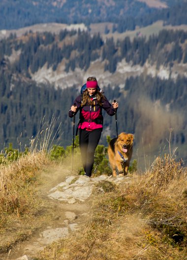 Woman hiking with dog on a mountain trail in autumn. | © Kleinwalsertal Tourismus eGen • Photographer: Lukas Rinner